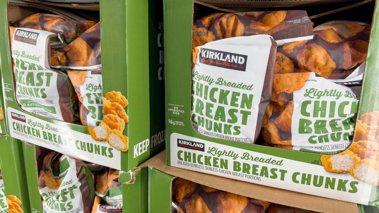 Cardboard boxes filled with bags of Kirkland lightly breaded chicken breast chunks are stacked.