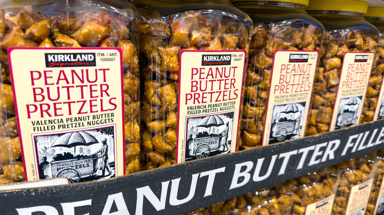 A row of clear plastic jars of Kirkland Signature peanut butter pretzels from Costco rest on a shelf.
