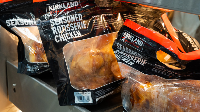 Three bags of Kirkland Signature seasoned rotisserie chicken rest on a metal shelf.