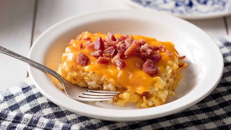 Loaded hash brown casserole on a plate with a fork on a black and white checkered tablecloth