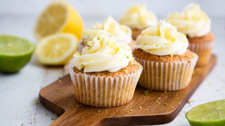 Lemon and poppy seed cupcakes with frosting sitting on a wooden cutting board
