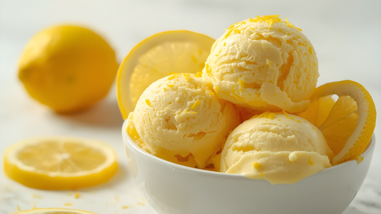 Creamy scoops of lemon ice cream with lemon slices and zest in a white bowl