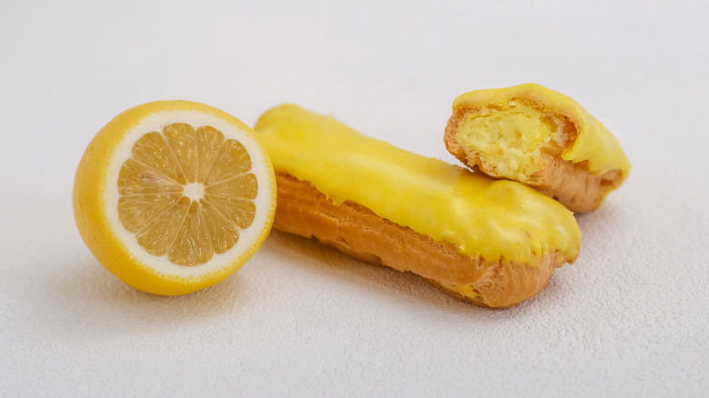 Eclairs with lemon filling under yellow glaze served alongside a half lemon