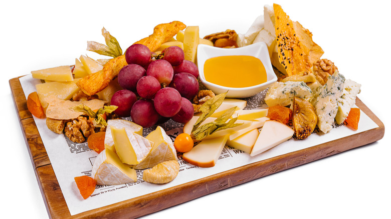 A cheese board with fruits, nuts, bread sticks, and a bowl of lemon curd for dipping