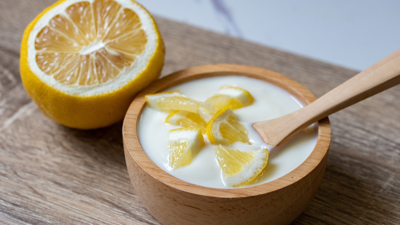 Lemon-flavored yogurt in a wooden cup and spoon with a slice and half of a lemon