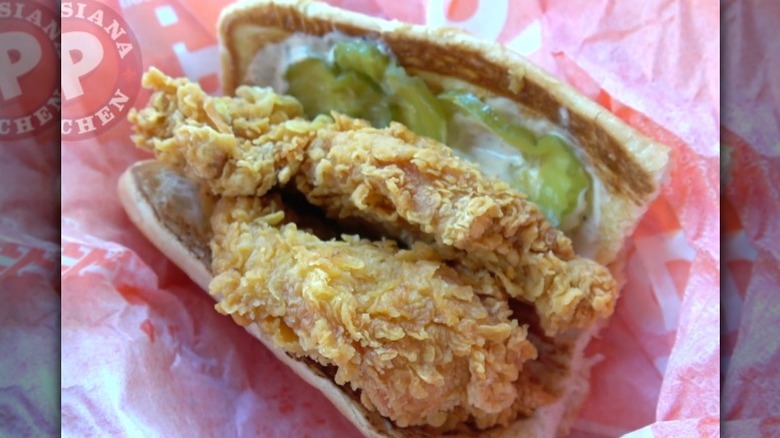 Screenshot from video of Popeye's Chicken Po' Boy with two pieces of fried chicken on bun with sauce and pickles