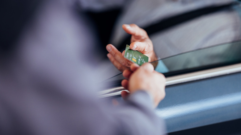 A credit card being handed from one hand to another from a car with the window rolled down