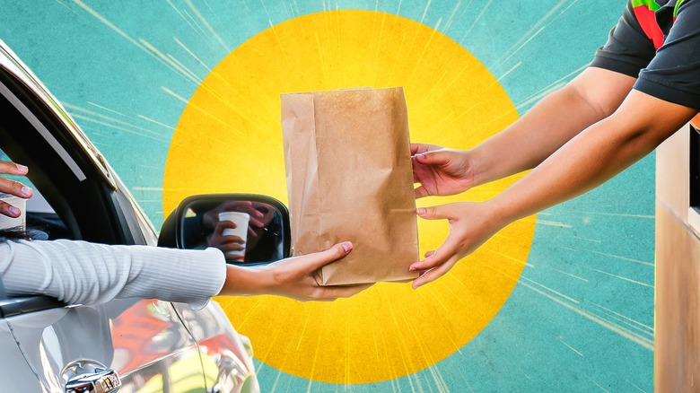 Drive-thru worker handing brown paper bag to woman in gray car against background of image of sun
