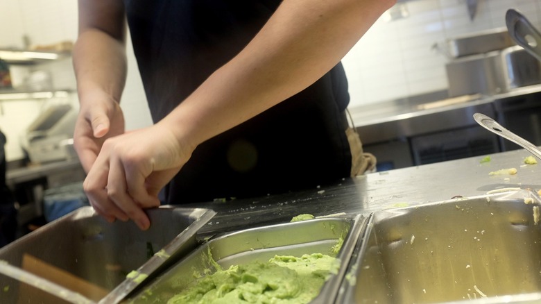 Worker emptying tub next to metal tub of guacamole