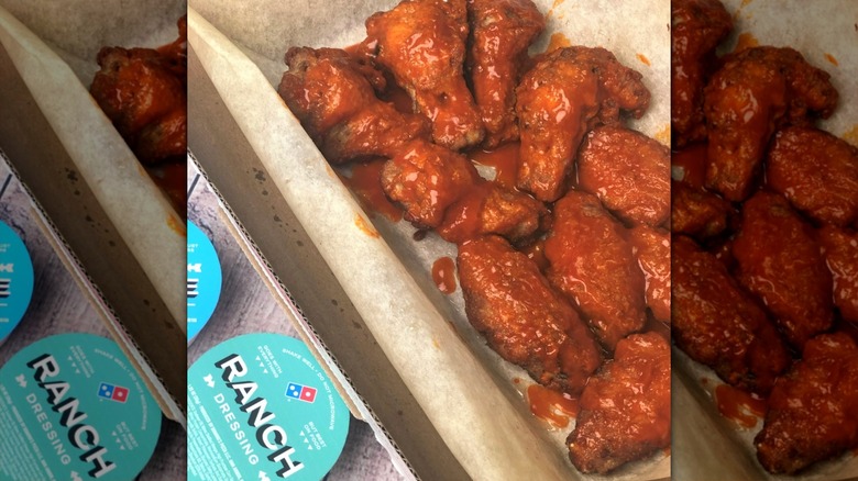 Domino's buffalo wings in a box next to tubs of dressing