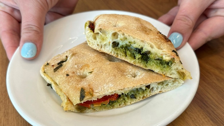 Hands with painted fingernails holding a plate featuring a split open Starbucks Tomato & Mozzarella Focaccia