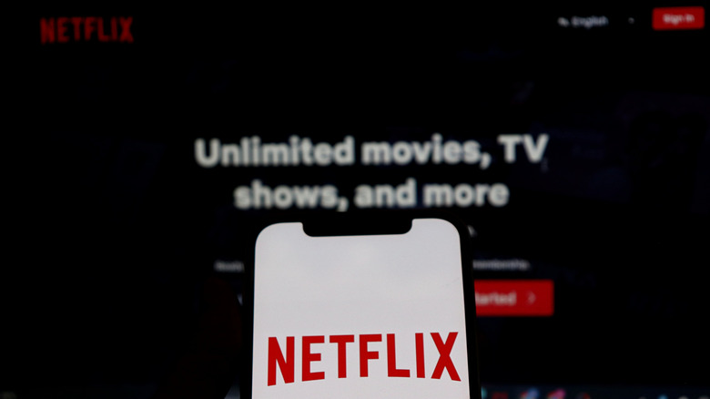 Netflix logo on a mobile device in front of a larger screen with the Netflix login page