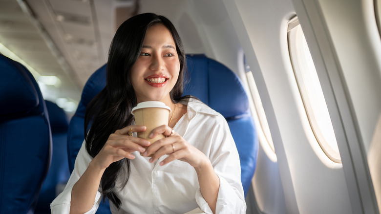 A woman drinking a hot beverage on a flight