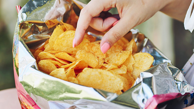 A woman reaching into a potato chip bag