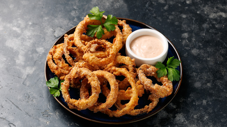 Onion rings on a black plate with sauce