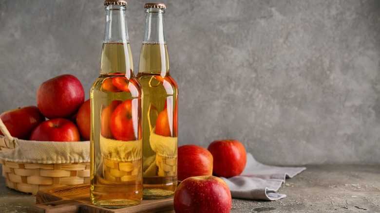 Bottles of fresh apple cider and a wicker basket filled with apples