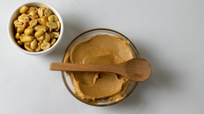 Peanut butter in a bowl with a spoon and a bowl of peanuts