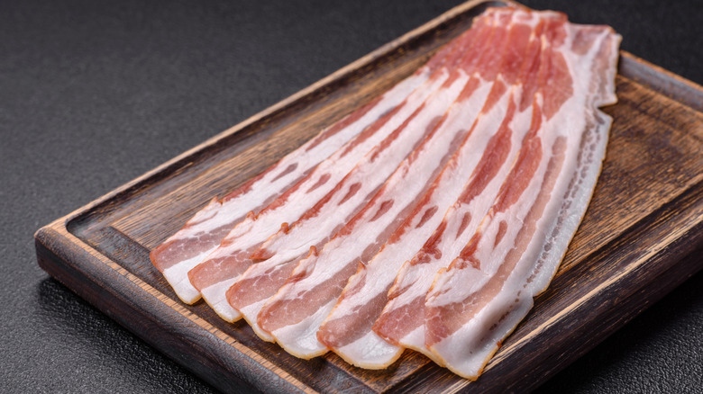 Raw slices of bacon on a wooden board