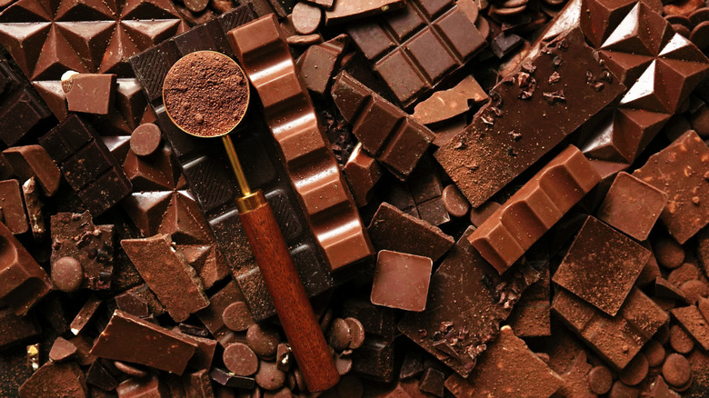 A pile of various chocolate candies with a scoop full of cocoa powder