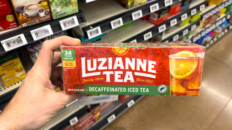 A hand holding a box of decaffeinated ice tea bags in a supermarket aisle