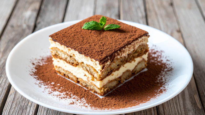 A slice of tiramisu on a white plate on a wooden table