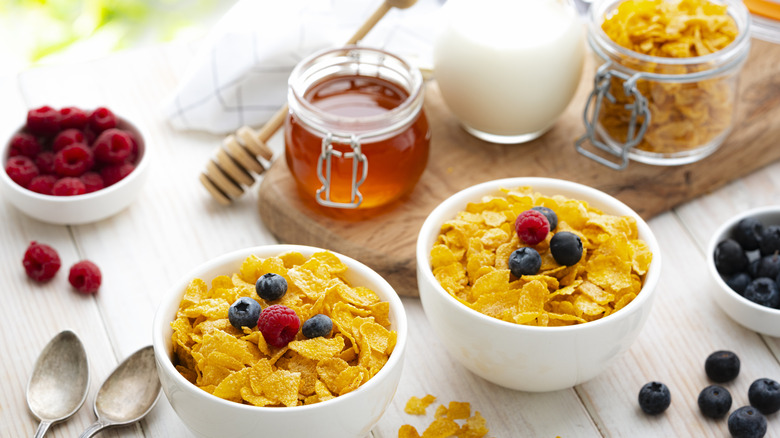 two bowls of cereal surrounded by berries and honey on white wooden table