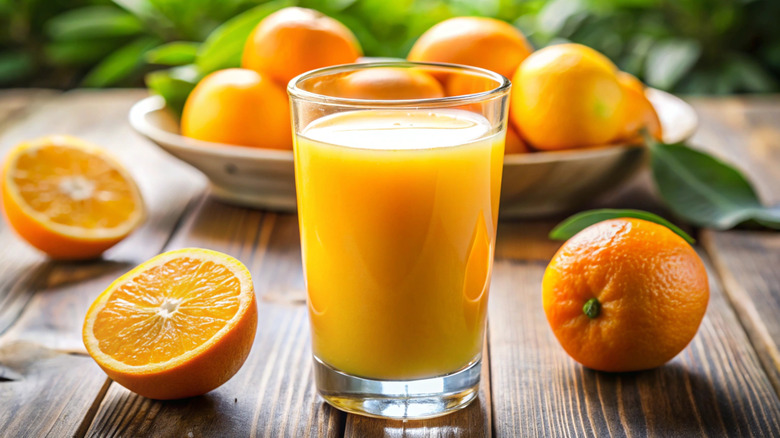 glass of orange juice with oranges in background on wooden table