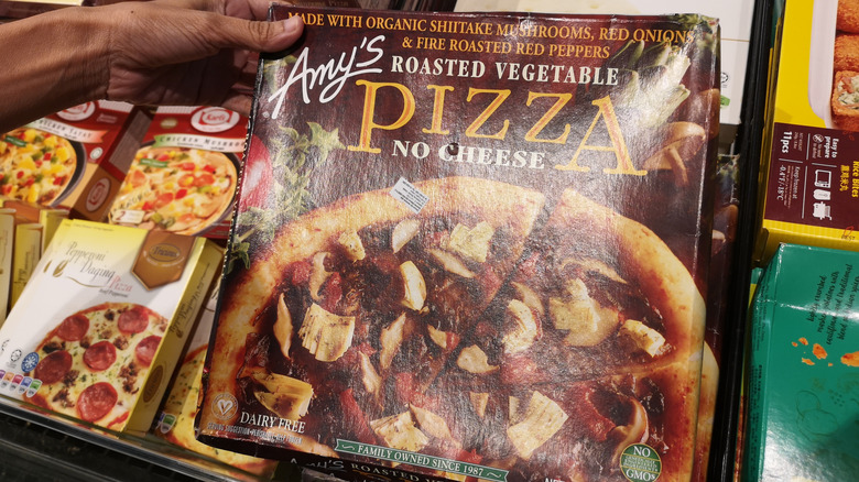 A hand holding an Amy's frozen pizza in a store