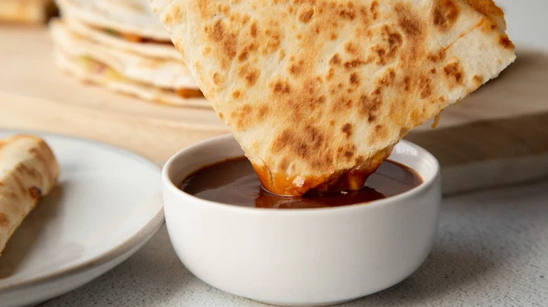 Quesadilla dipped in bowl of sauce