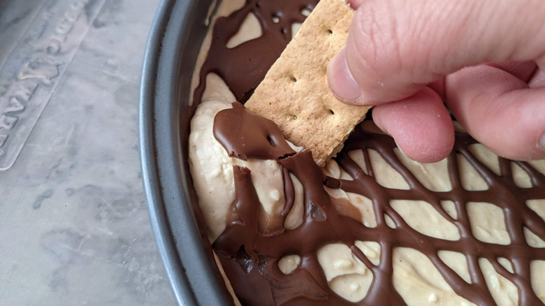 hand dipping graham cracker in peanut butter chocolate