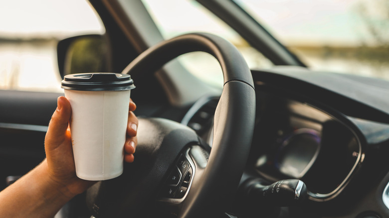 Someone driving with a cup of coffee in their hands.