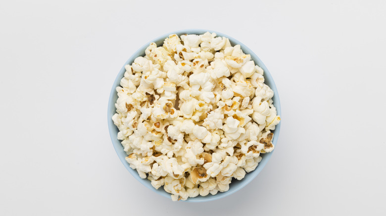 Tasty popcorn in bowl on color background, top view