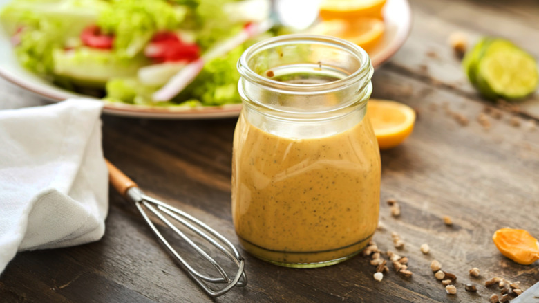 homemade salad dressing in a jar next to a bowl of salad