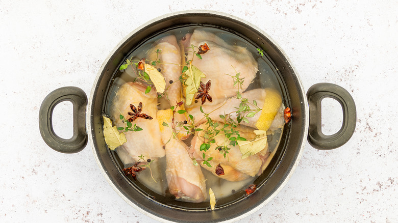 Fresh organic chicken in a pot with a brine solution of lemon peel, fresh thyme, peppercorns, star anise, salted water, and sugar