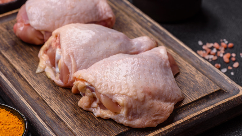 Fresh raw chicken thighs with salt and spices on a wooden board