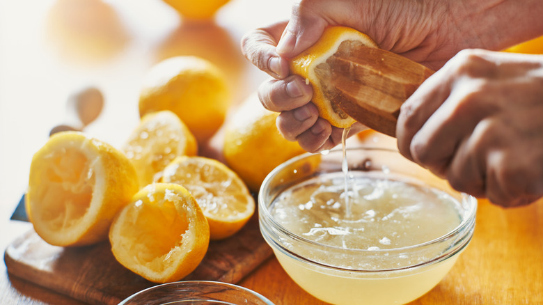 Person's hand squeezing juice from a lemon with wooden tool
