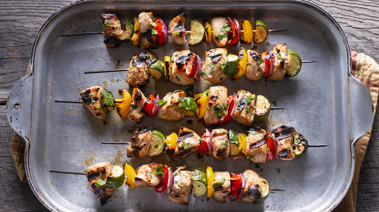 Grilled chicken kebabs with red and yellow bell peppers, zucchini, and red onion on a pan