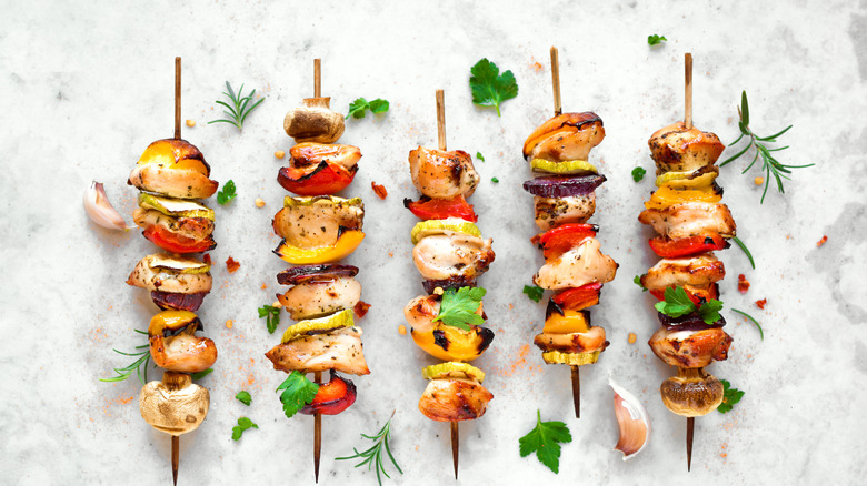 Grilled vegetable and chicken skewers with bell peppers, zucchini, onion, and mushrooms on white marble background