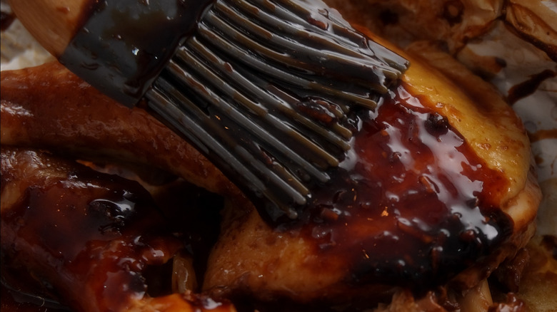Glazing raw chicken leg with teriyaki sauce close-up
