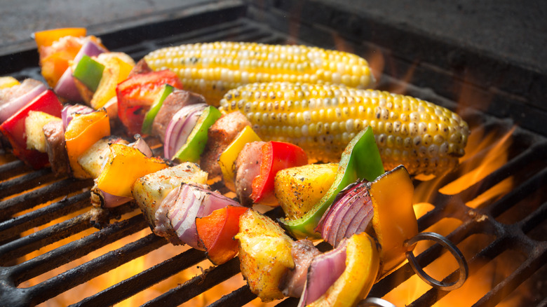 Chicken kebabs on a grill with corn on the cob