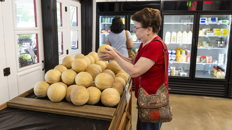 A woman shopping for cantaloupe in supermarket