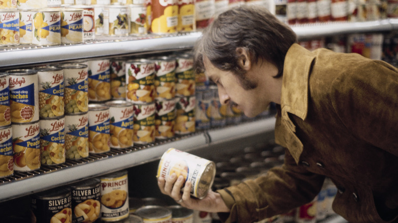 A man holding a canned product in a supermarket, 1970s