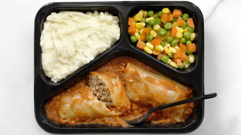 a frozen dinner tray with mixed vegetables, mashed potatoes, and stuffed cabbage rolls in red sauce