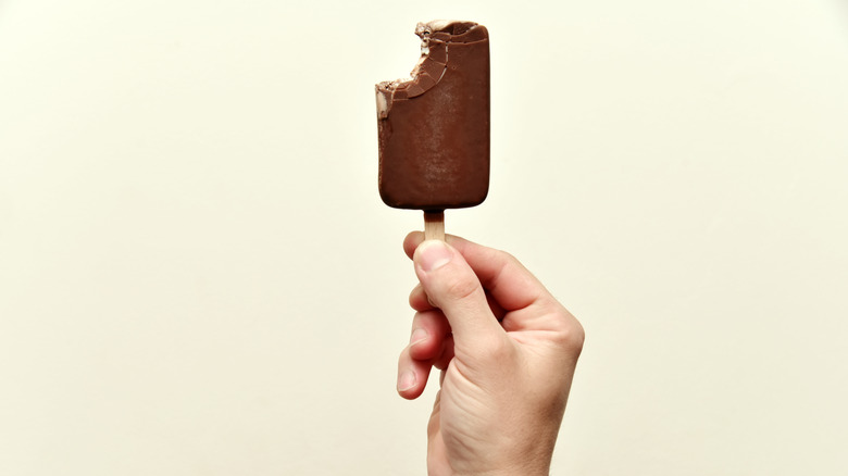 hand holding a bitten-into ice cream bar on a stick
