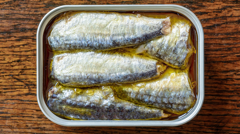 An open can of sardines in oil on a weathered wooden table seen from above.
