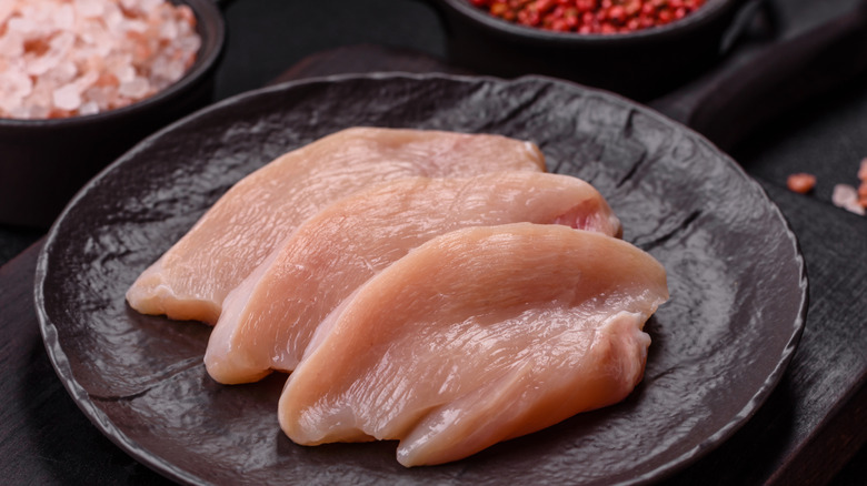 Fresh chicken fillet on a dark concrete table with spices and herbs.