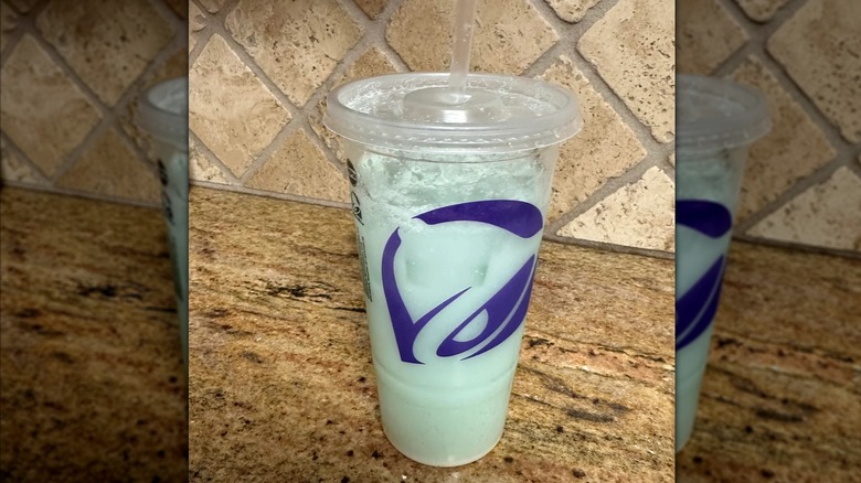 Taco Bell Mountain Dew Baja Blast Dirty Soda Freeze in a cup sitting on a fake wood surface.