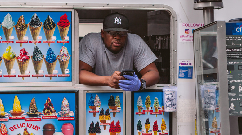 An ice cream seller hanging out of the window of an ice cream truck