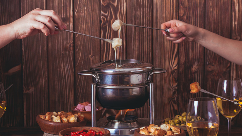 A cheese fondue pot with other dishes and people dipping food