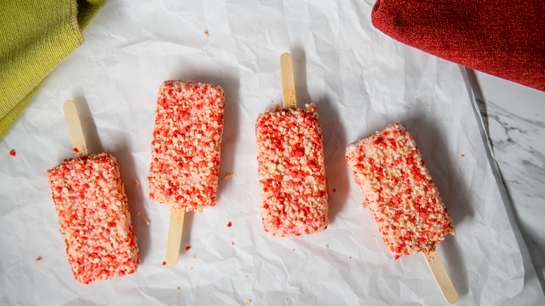 Four Strawberry shortcake ice cream bars with cake crumbles laying flat on parchment paper